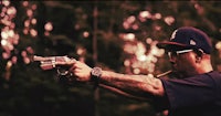 a man with tattoos holding a gun in the woods